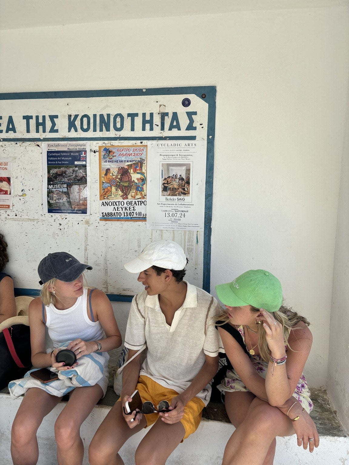 Three people sitting against a white wall in Greece